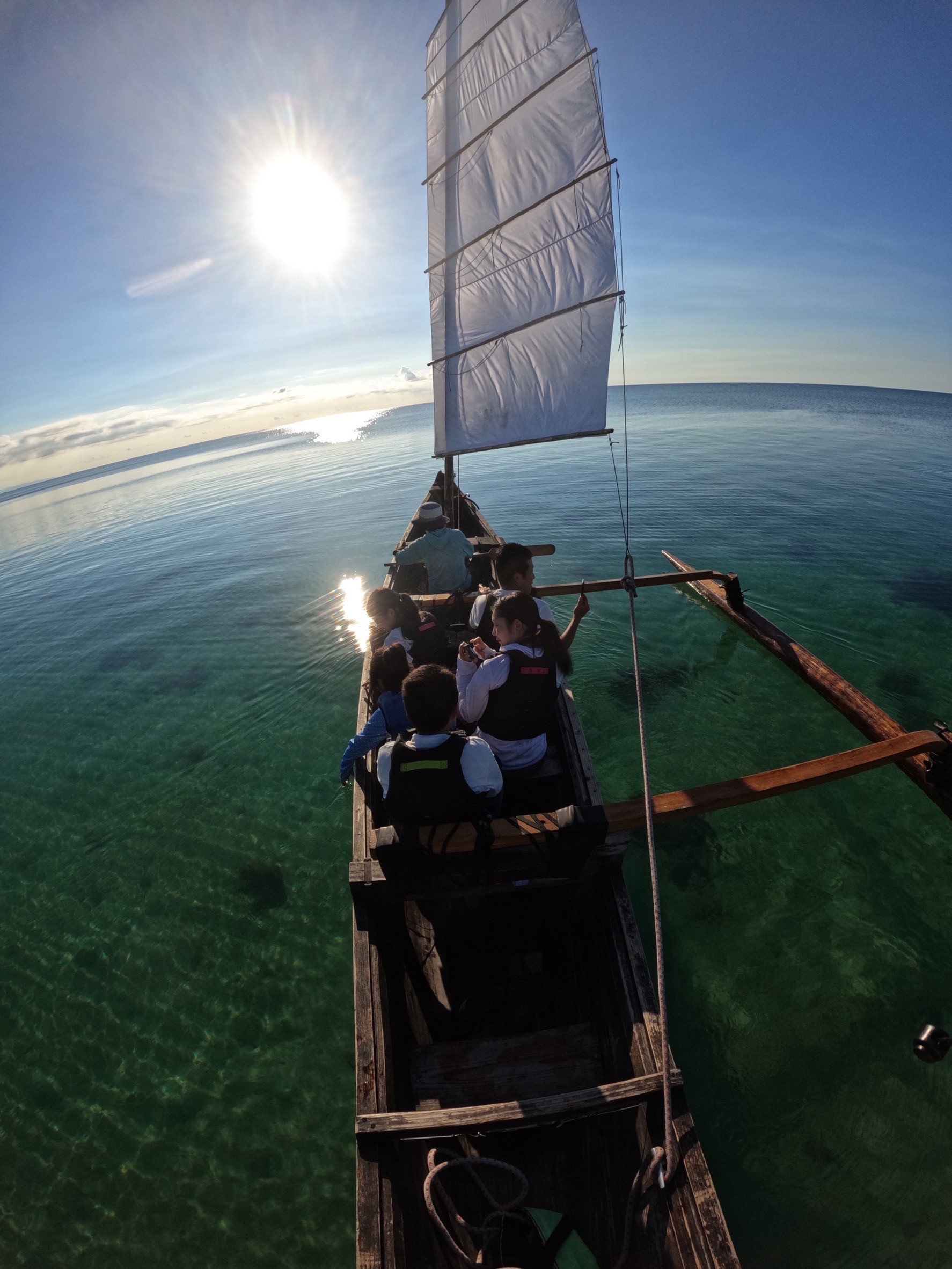 石垣島の明るい日差しの下、地元の工芸品や農産物を販売する魅力的な店のガラスドアに、笑顔の店主が「平久保半島認定」のステッカーを誇らしげに貼っている様子